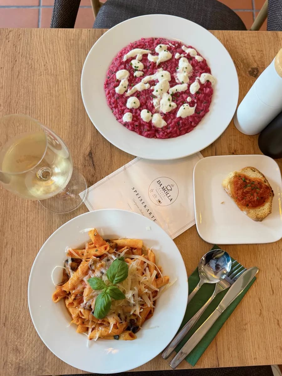 Rote-Bete-Risotto, Pasta mit Tomatensauce und Parmesan, Bruschetta und ein Glas Weißwein auf einem Holztisch